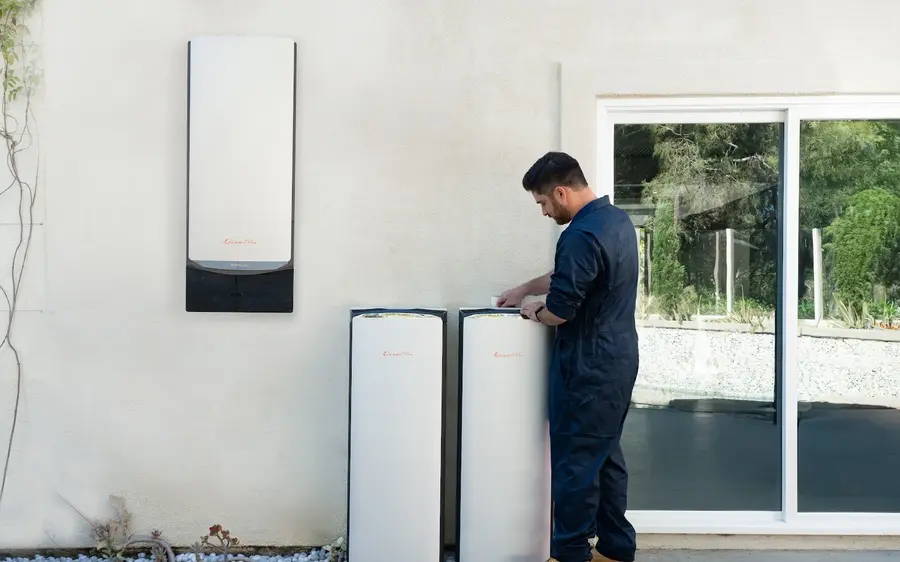 An EcoFlow Ocean Pro battery installation on an exterior wall, with a technician working at the two floor standing battery modules.