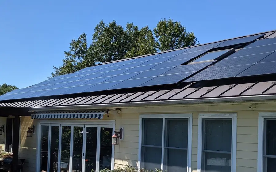 All black solar electric modules on a standing seam metal roof, seen from the ground beside the house.