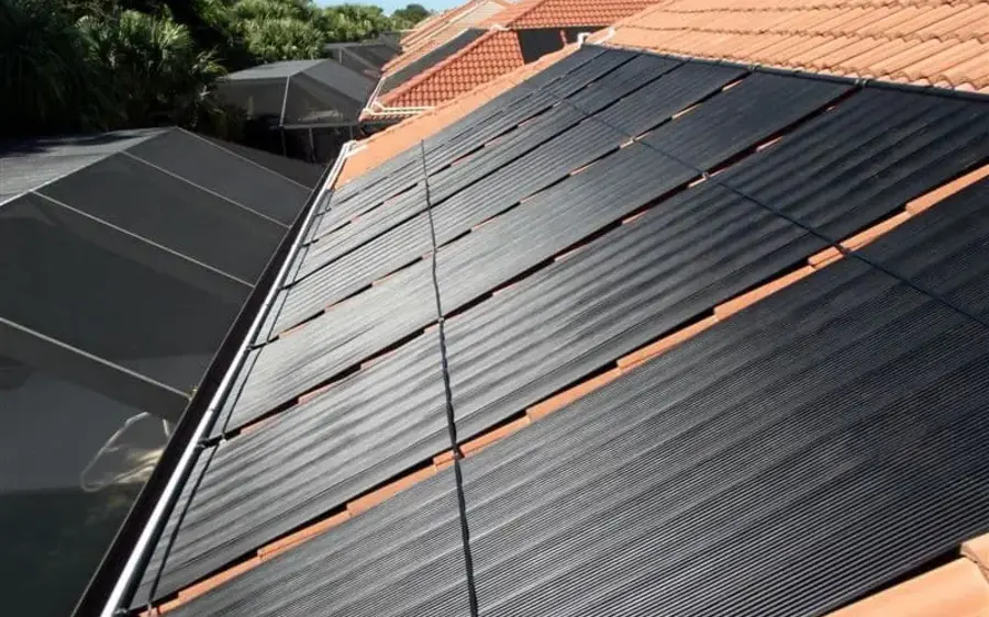 Solar pool heating collectors on a tile roof, with the header pipe running horizontally across the top of the panel bank.